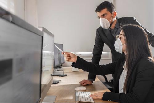Two people wearing masks look at a computer monitor.